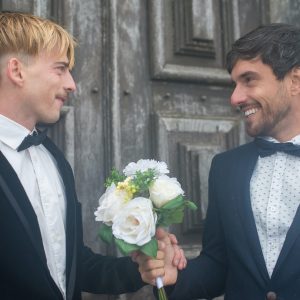 Rainbow newlyweds in dark suit with groom bouquet